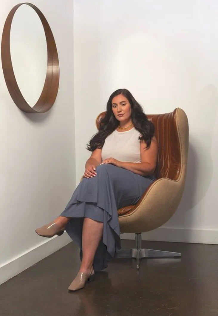 Curve Model, Sarah, is pictured seated and wearing LISA AVIVA's Batwing Sleeve Top, in Singing Sands and the Wool Joggers, in Rocky Mountain Skies