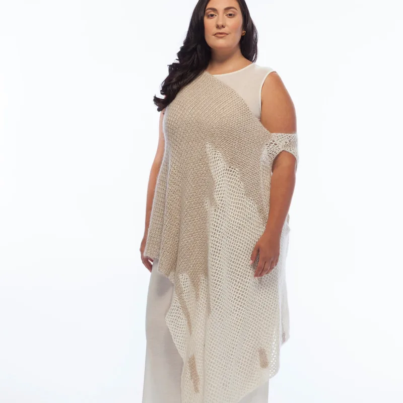 Curve model, Sarah, is pictured against a white wall, wearing LISA AVIVA's Column Dress, in Cream - topped with the Hand Crocheted Poncho in Baby Camel and Cream.